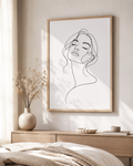 Serene Muse minimal line art print — large framed wall art of a woman's face with eyes closed and flowing hair, hung above a wooden sideboard with dried flowers and ceramic bowls in a bright Scandinavian bedroom, Morphē Studio