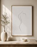 Soft Silhouette minimal line art print — framed wall art with a single curved line of a woman's body, hung above a marble console with large ceramic vase, olive branch and stacked books in a warm Scandinavian interior, Morphē Studio