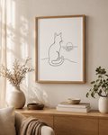Sunset Watcher minimal line art print — framed wall art of a cat watching the sunset by the sea, hung above a wooden sideboard with ceramic vases, dried flowers and stacked books in a warm Scandinavian living room, Morphē Studio